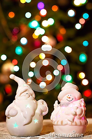 Illuminated Snowman and Jack Frost (Santa Claus) dolls in front of Christmas tree lights, blurred background Stock Photo