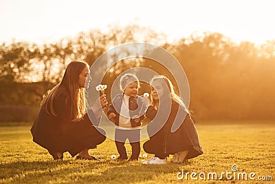 Illuminated by sunlight. Playing with dandelion. Woman with her two young daughters is on the summer field Stock Photo