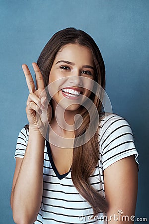 Im diggin your vibes. Studio shot of an attractive young woman making a peace gesture against a blue background. Stock Photo