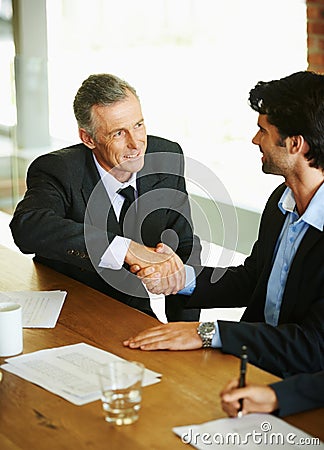 Im looking forward to doing business with you. Two businessmen seated at a table and shaking hands. Stock Photo