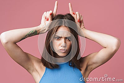 Image of angry brunette woman holding fingers on her head like devil horns Stock Photo