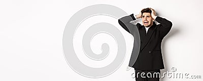 Image of anxious businessman start to panic, looking left with worried expression, standing in black suit over white Stock Photo