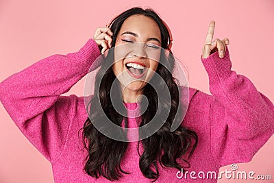 Image of asian girl pointing finger and listening to music with headphones Stock Photo