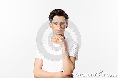 Image of attractive gay man in white t-shirt, having glitter on face and looking at camera serious, standing over white Stock Photo