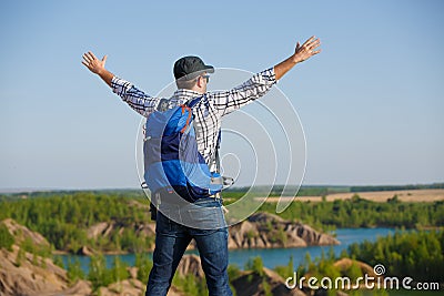 Image back of tourist man with backpack ,hands up on hill in background of mountain expanses, blue sky Stock Photo
