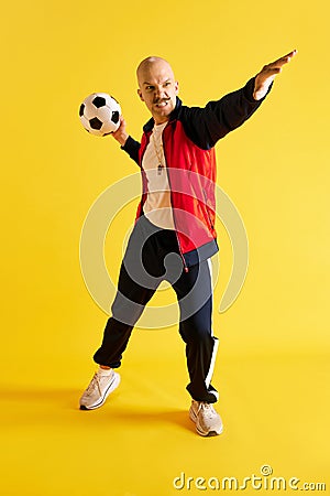 Image of balded and mustache angry young sport coach with soccer ball over yellow studio background. Stock Photo