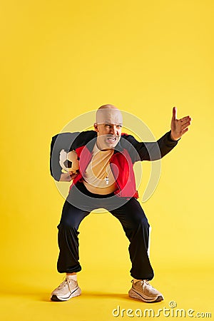 Image of balded and mustache young trainer with soccer ball over yellow studio background. Stock Photo