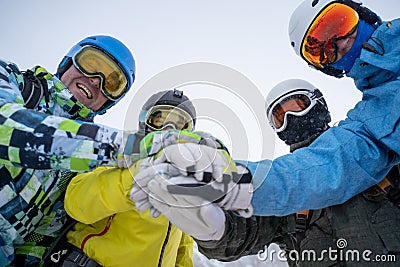 Image from bottom of four happy snowboarders in helmet doing handshake Stock Photo