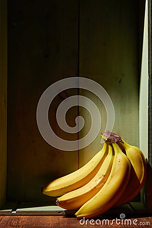 Image of bunch of ripe yellow bananas on wooden background, bright sunlight, harvest in wooden box Stock Photo