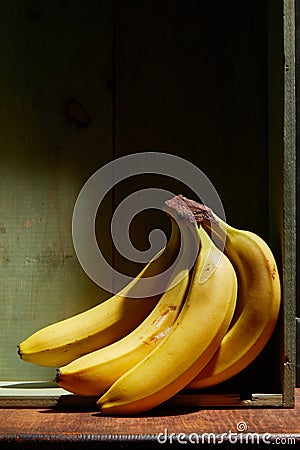 Image of bunch of ripe yellow bananas on wooden background, bright sunlight, harvest in wooden box Stock Photo