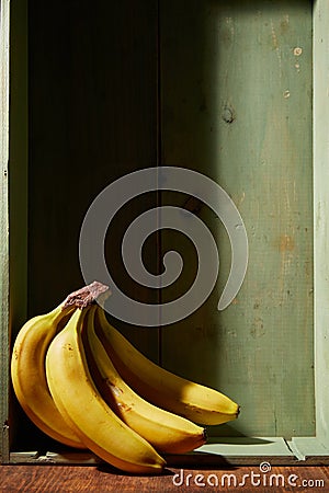 Image of bunch of ripe yellow bananas on wooden background, bright sunlight, harvest in wooden box Stock Photo