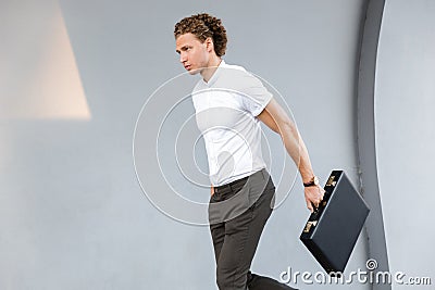 Image of Calm curly business man with briefcase walking Stock Photo