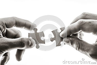 The image captures two hands, one belonging to an adult and the other to a younger individual, each holding a puzzle Stock Photo
