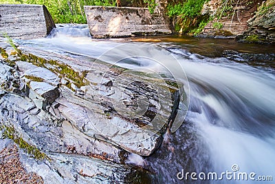 Cement dam funneling river with large outcropping of stone covered in moss Stock Photo