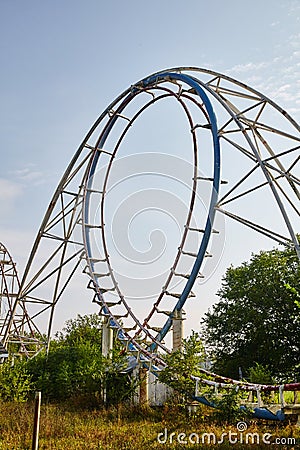 Centered shot of a blue rollercoaster surrounded by trees on a clear grayish day Stock Photo