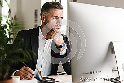 Image of confident businessman working in office and looking on computer Stock Photo