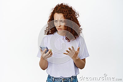 Image of confused redhead woman cant understand how to use application, bad user experience with smartphone app, looking Stock Photo