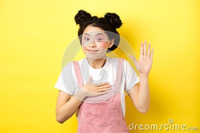 Image of cute asian girl with makeup being honest, raising hand and put on heart, telling truth, give oath and smiling Stock Photo