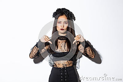 Image of disappointed asian woman in halloween dress of gothic undead girl showing thumbs-down, dislike and disagree Stock Photo