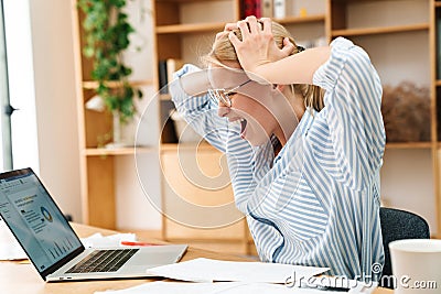 Image of displeased woman grabbing her head while working with laptop Stock Photo