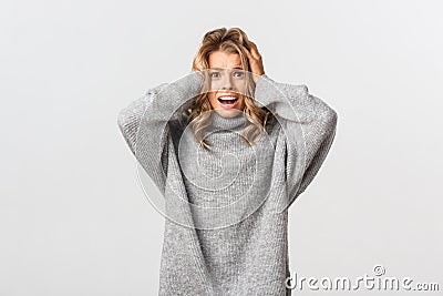 Image of distressed and worried blond girl holding hands on head, panicking and looking at camera concerned, standing Stock Photo