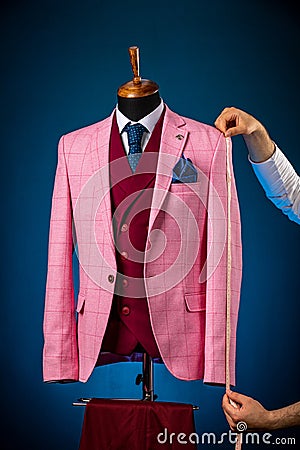 Image of dressmaker or tailor using tape measure on mannequin or dummy with suit at fashion studio Stock Photo