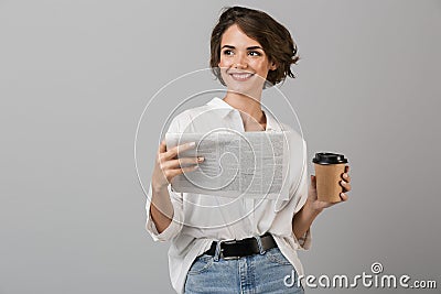 Emotional young business woman posing over grey wall background reading newspaper drinking coffee Stock Photo