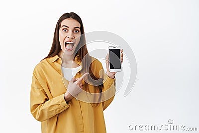 Image of excited woman checking out cool new online promo, pointing at smartphone and scream from joy and amazement Stock Photo