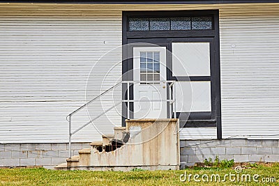 Exterior white house with white door with stained glass mosaic windows and busted concrete steps Stock Photo