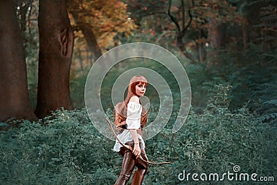 Image of a forest hunter, an attractive girl with long red hair in a white shirt and leather pants goes hunting, holds a Stock Photo