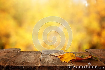 image of front rustic wood table with dry gold leaves and fall bokeh background. Stock Photo