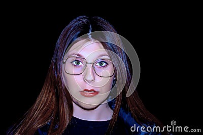 Image of girl with black background illuminated by blue light with glasses and interrogative expression long hair. Stock Photo