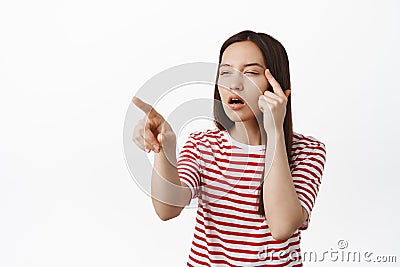 Image of girl cant see without glasses, squinting eyes and pointing at smth, trying to reed without eyewear, standing in Stock Photo
