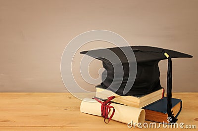 Image of graduation black hat over old books next to graduation on wooden desk. Education and back to school concept. Stock Photo