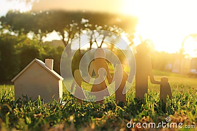Image of happy family concept. wooden cut people holding hands together next to home in green grass during sunset. Stock Photo