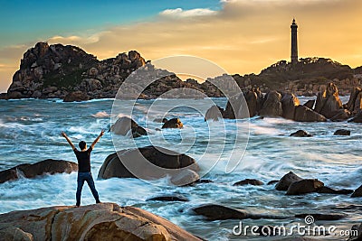 A Happy Man Celebrating Victory on The Top of A Big Rock by The Ocean Stock Photo