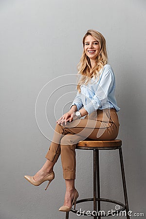 Blonde business woman posing isolated grey wall background sitting on stool Stock Photo