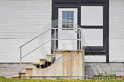 House with white siding and door with black frames and busted concrete stairs Stock Photo