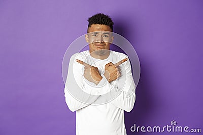 Image of indecisive african-american guy, uncomfortable making decision, asking for help with choice, pointing fingers Stock Photo