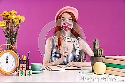 Image of joyful teenage girl holding paper flower on stick while studying with exercise books at desk Stock Photo