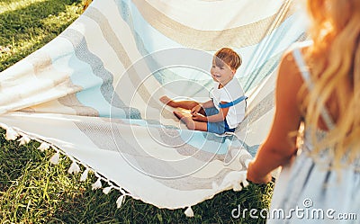 Image of little brother and his sister playing with the blanket on green grass. Happy little boy and little girl having fun and Stock Photo