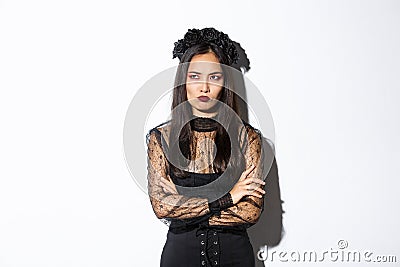 Image of mad asian woman in gothic lace dress and wreat, cross arms chest, frowning and sulking while looking angry at Stock Photo