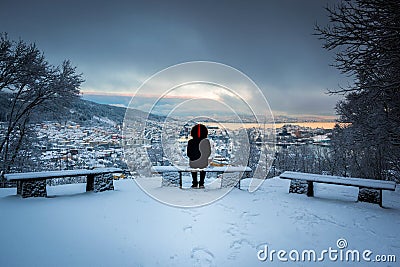 Winter Scene with A Lone Man Sitting on Snowy Benches Overlooking Bergen City Center in A Storm Stock Photo