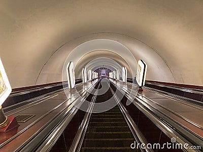 An image of a moving escalator with reflective surface, handrails, and lighting fixtures, inside a tunnel-like structure Editorial Stock Photo