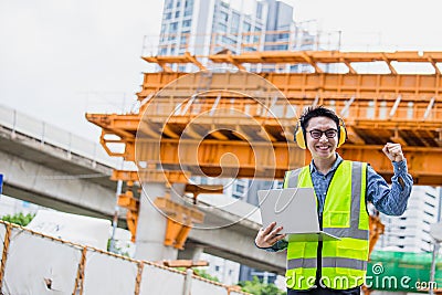 Image outside the industrial construction engineers in yellow protective ear muff discuss new project while using laptop and happy Stock Photo