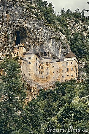Image of Predjamski castle with trees in the foreground Stock Photo