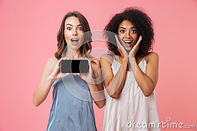 Pretty shocked young two women showing display of mobile phone. Stock Photo