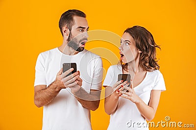 Image of puzzled couple man and woman using smartphones together, isolated over yellow background Stock Photo