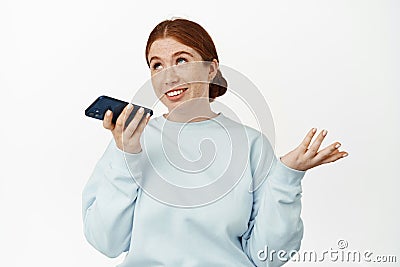 Image of redhead caucasian girl record voice message, talking on speakerphone, gesturing and chatting on mobile app Stock Photo