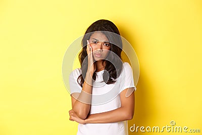 Image of sad and gloomy african american girl, looking upset and pouting, feeling frustrated while standing over yellow Stock Photo